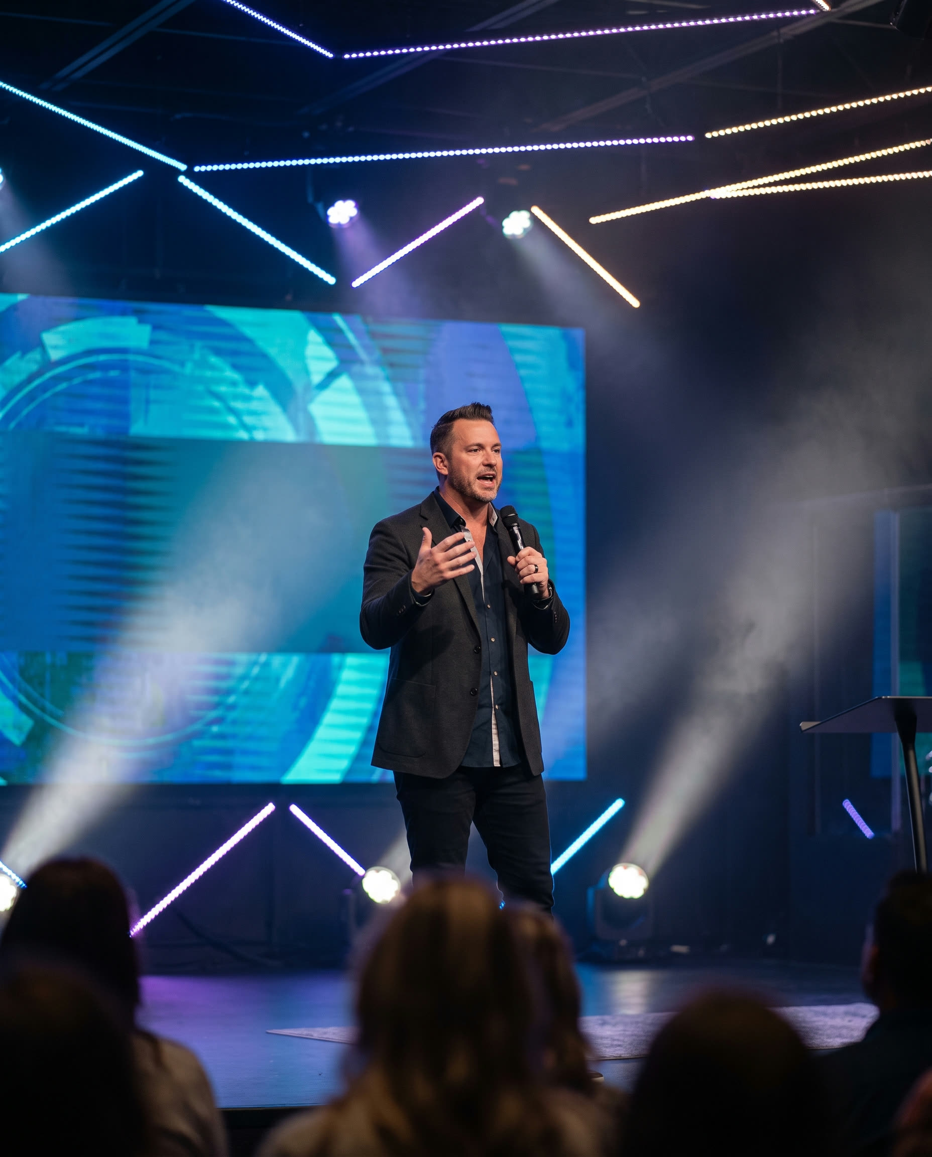 Pastor speaking on stage with a blurred blue graphic backdrop